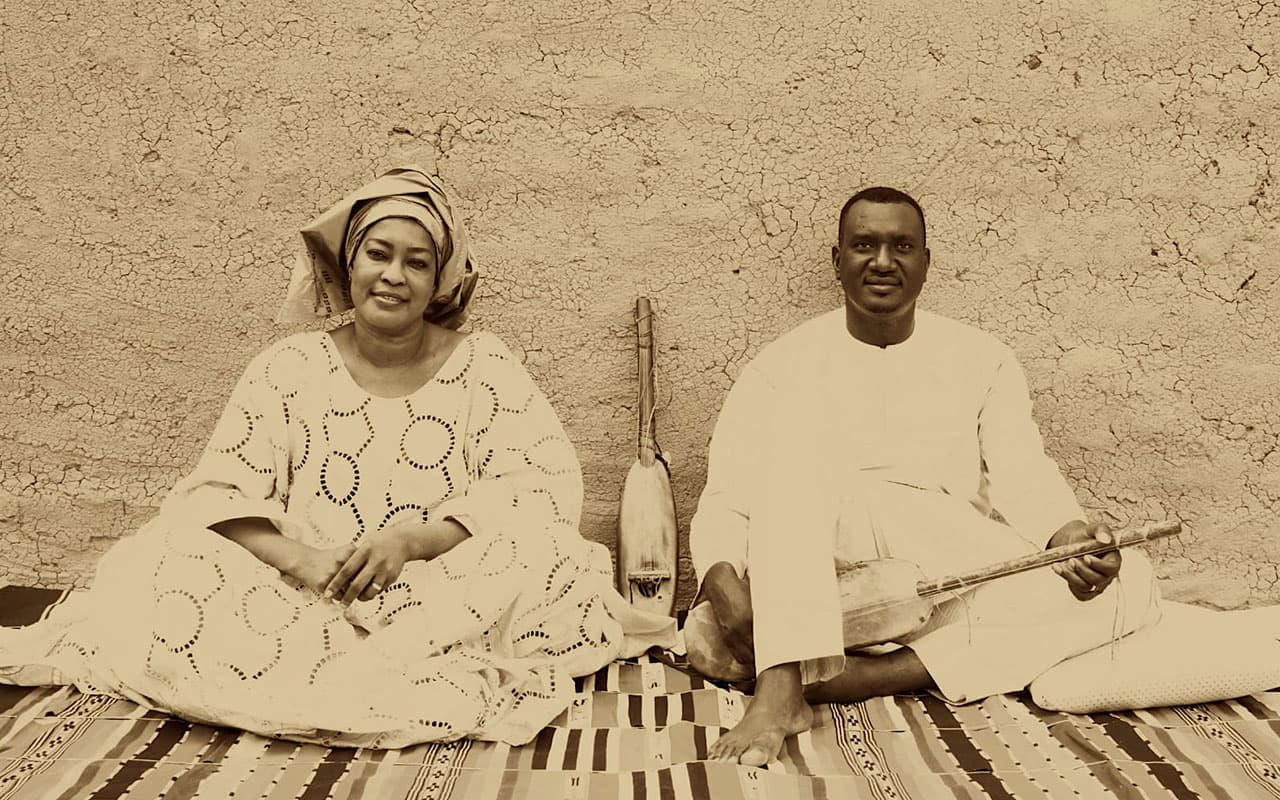 A man and woman sit on the floor with an instrument between them