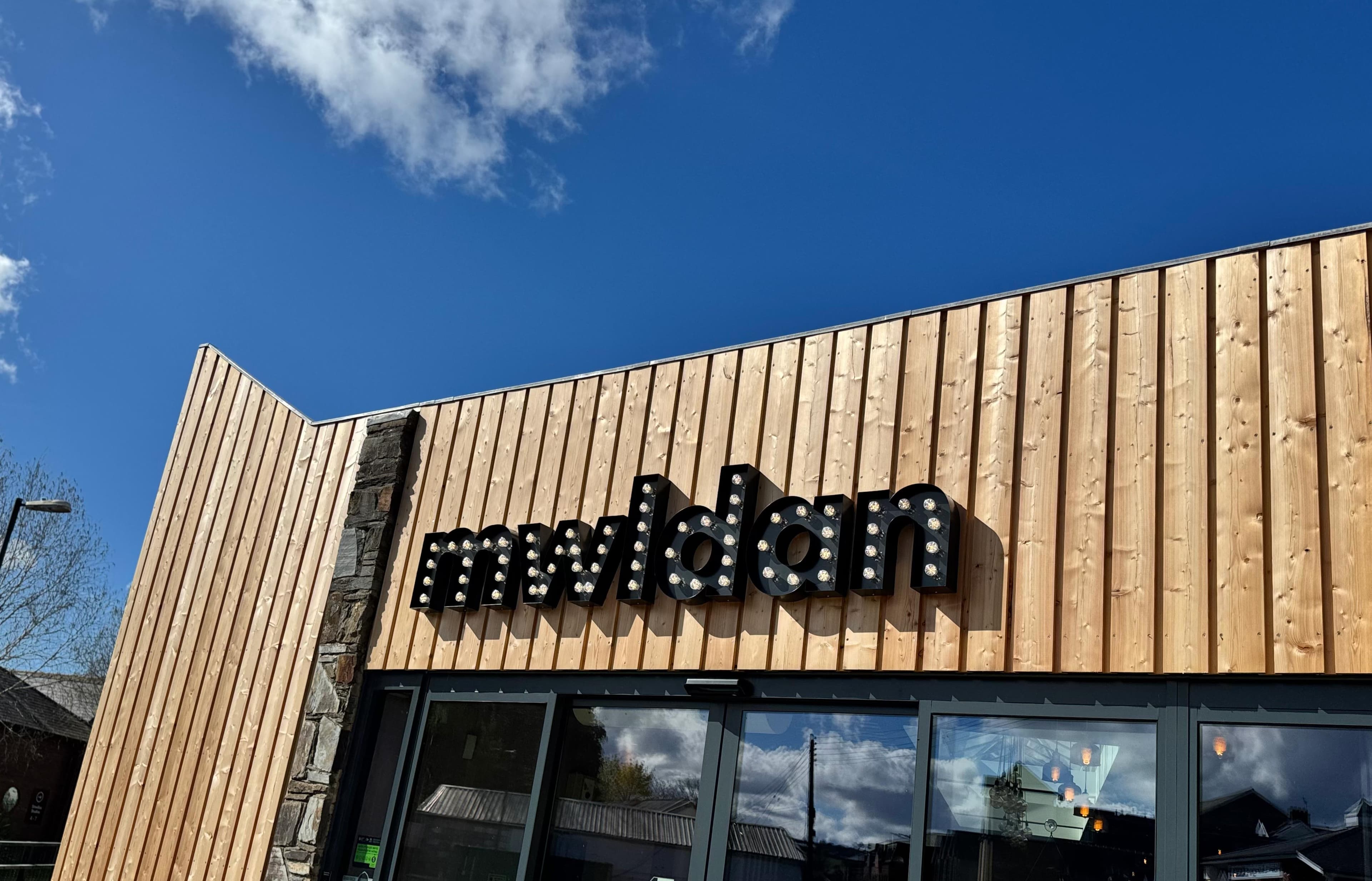 Mwldan's wooden clad fascia on a sunny day with the word Mwldan lit up in light